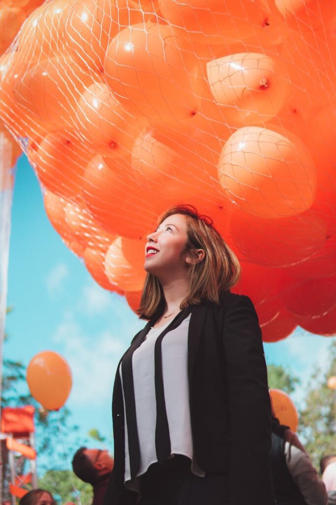 zipwp-image-1919226 Woman in Black Cardigan Smiling Under Orange Balloons